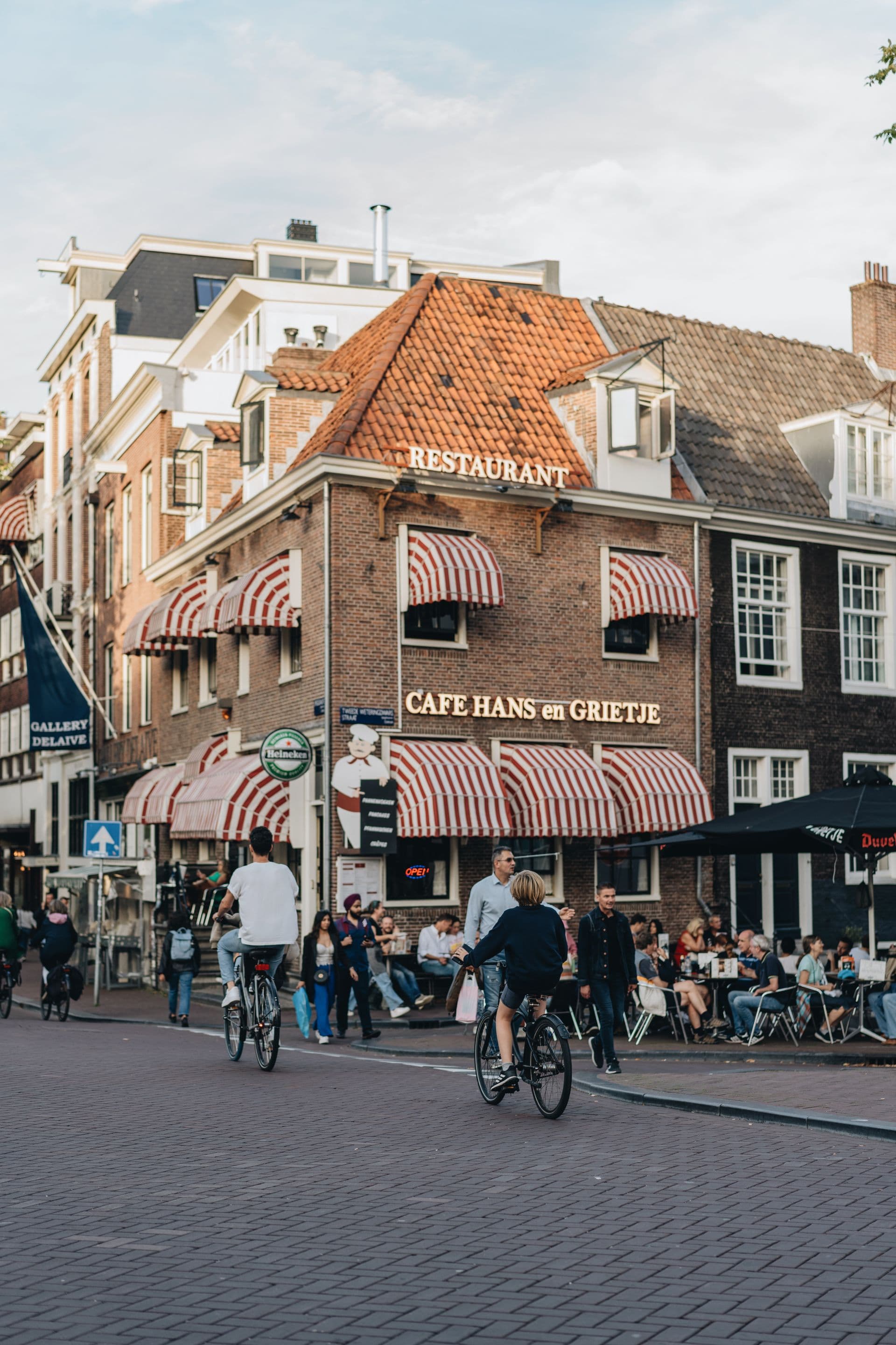 Restaurant met rood-witte markiezen en een vol terras op een Amsterdamse straathoek