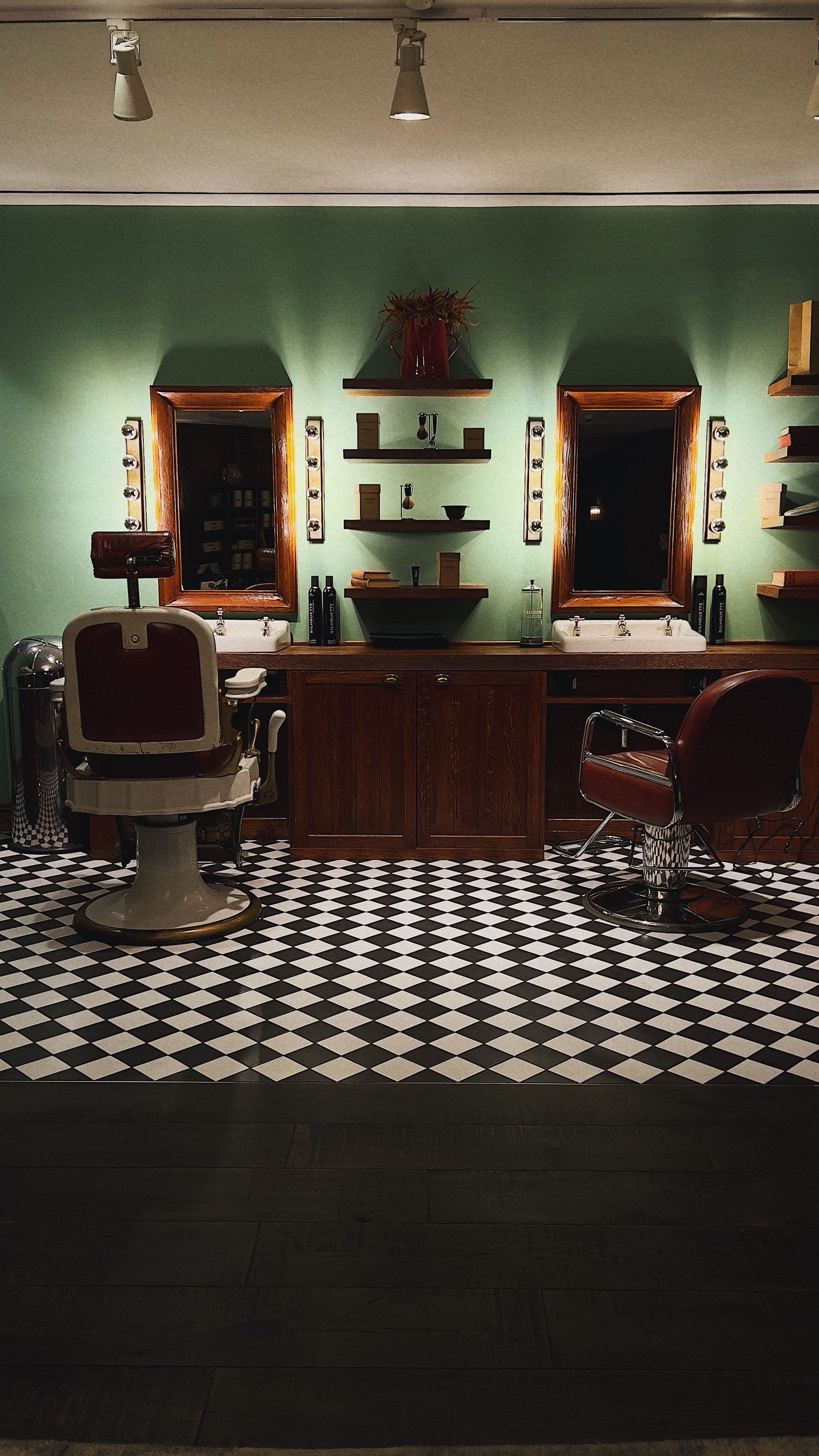 Kapsalon met vintage kappersstoelen, verlichte spiegels en een zwart-wit geblokte vloer
